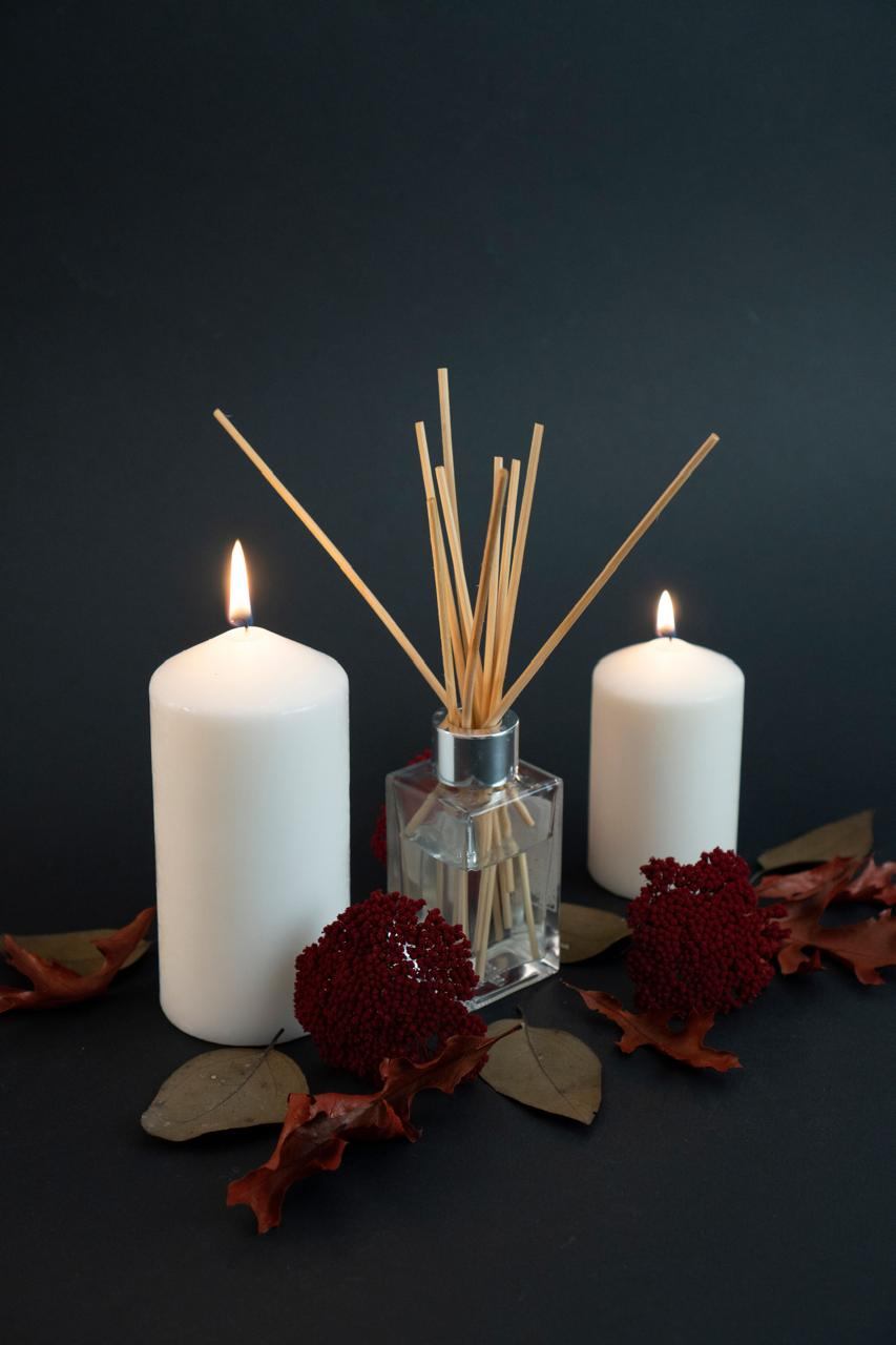 A reed diffuser between two white pillar candles