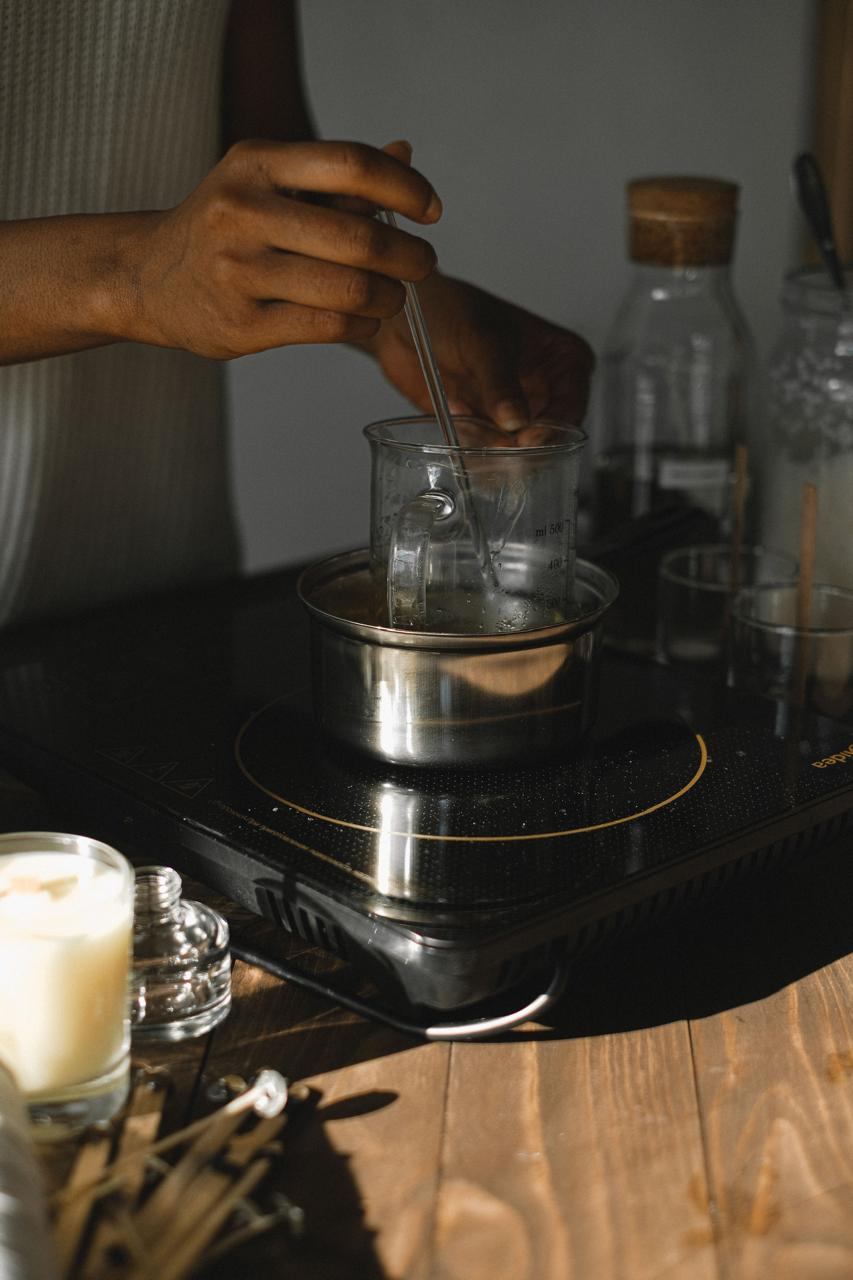 Hands stirring melted soy wax in a glass jug