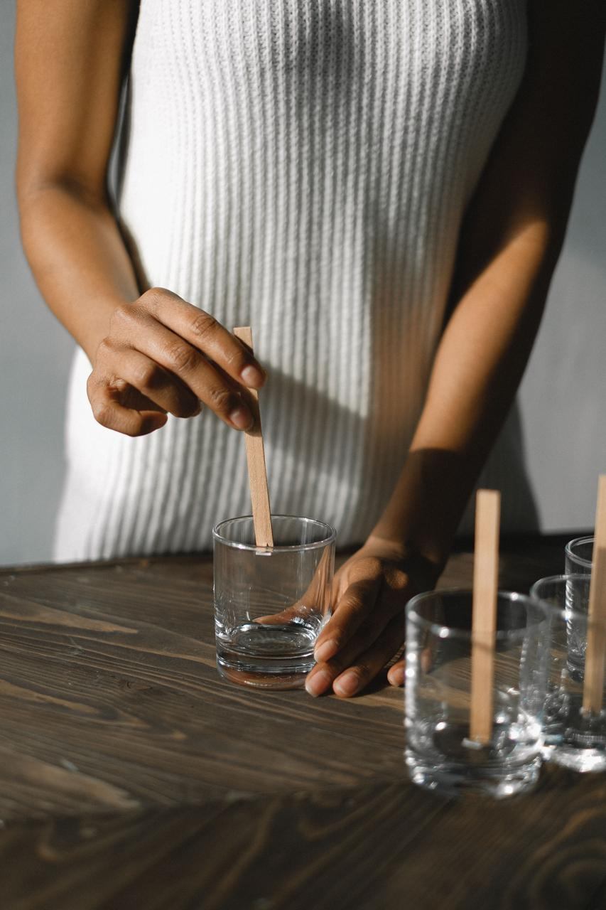 A wooden wick being placed into a glass candle vessel